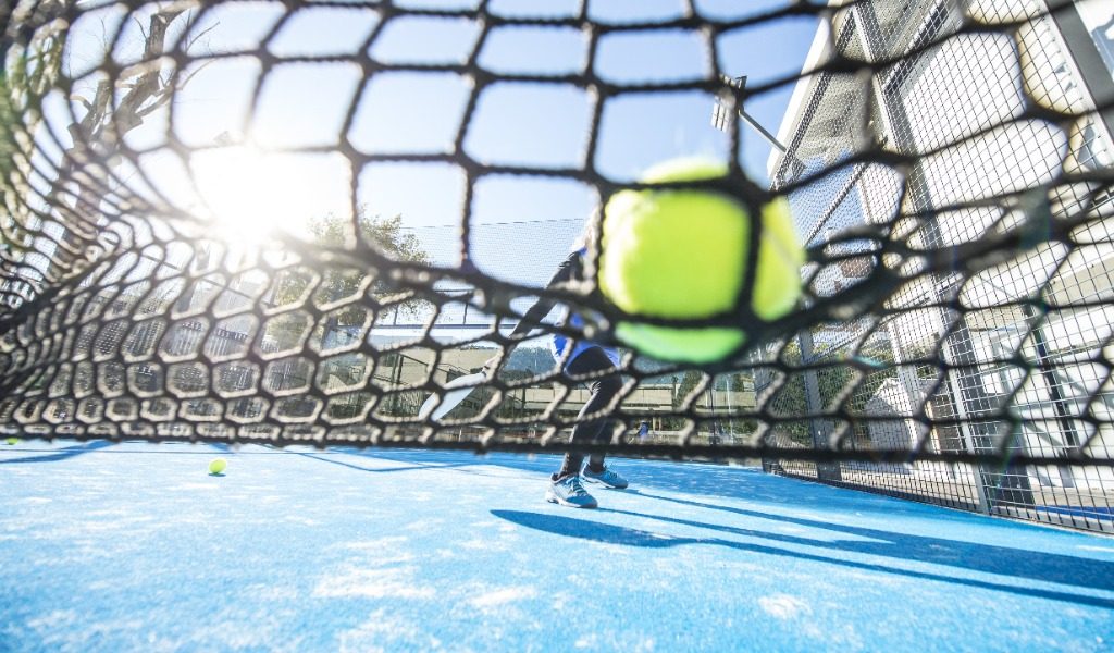 Padelspeler slaat een onderhands opslag op een groene padelbaan